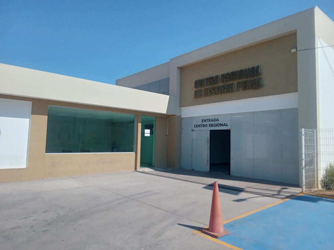 Fachada beige y blanca de edificio con letrero Centro Regional de Justicia Penal y cono de seguridad.